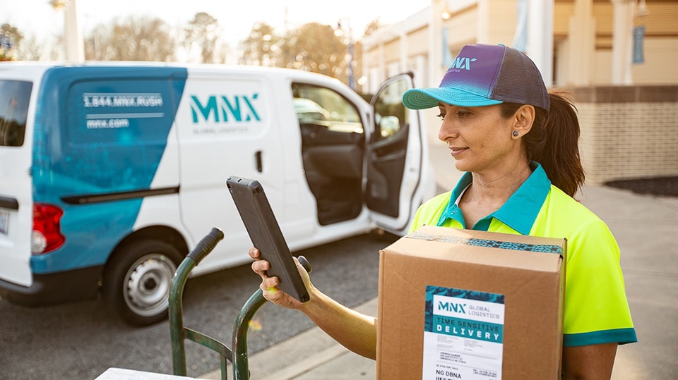 MNX Global Logistics delivery driver holding a parcel in front of a van